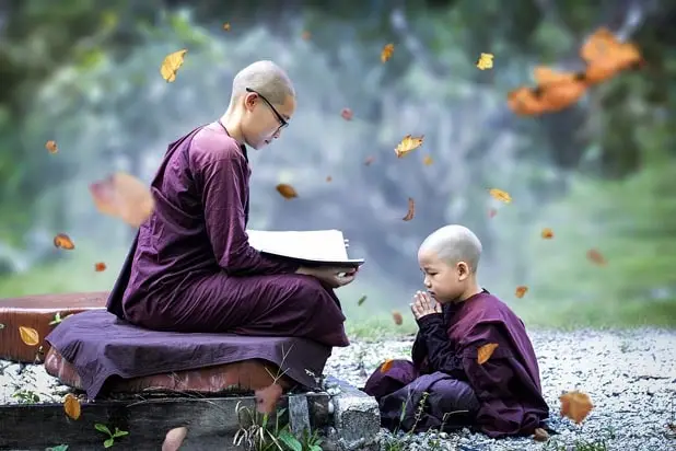 Buddhistischer Lehrer mit seinem Schüler in der Natur auf einer Bank sitzend